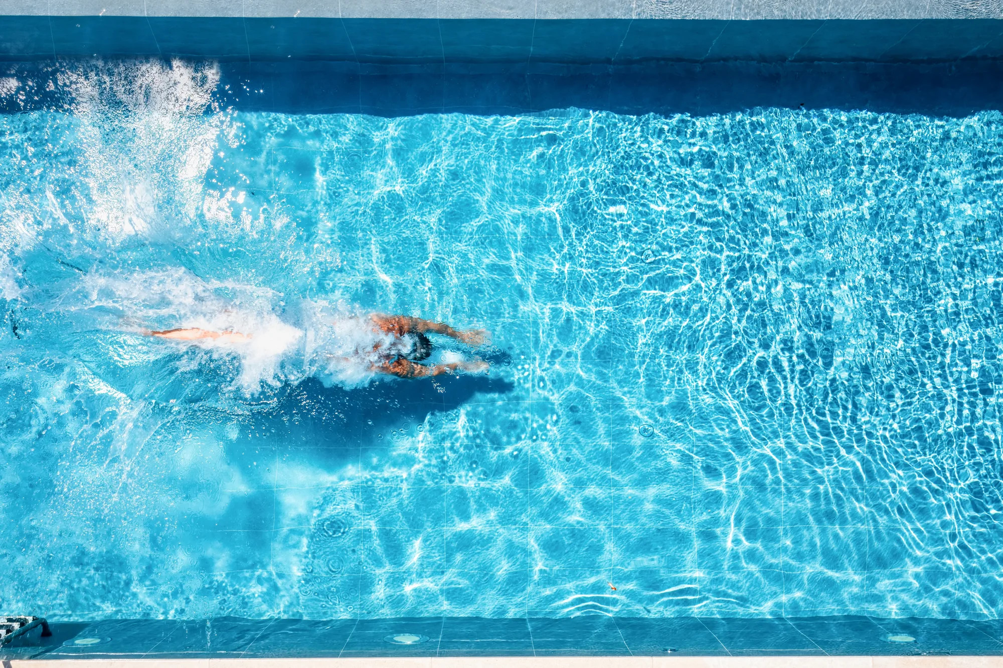 A swimmer diving into clear blue pool water, seen from above
