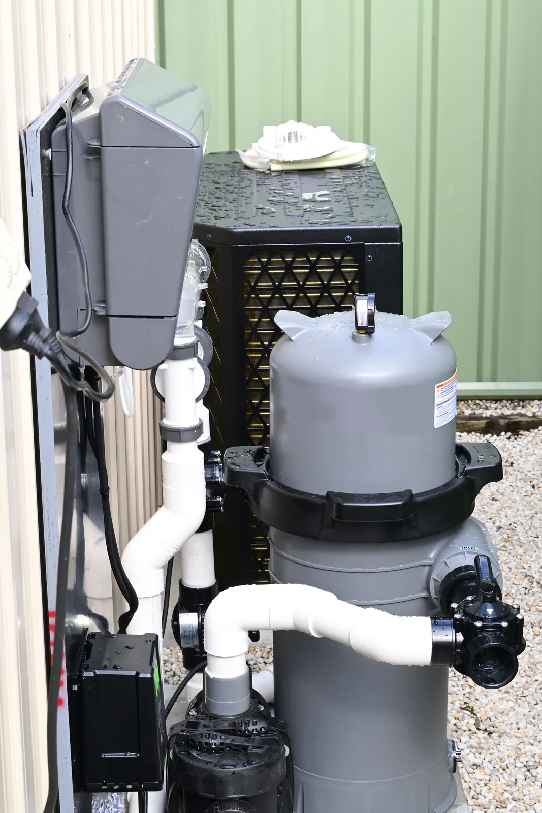 Pool equipment beside a house: a pump, a filter and a chlorinator control box