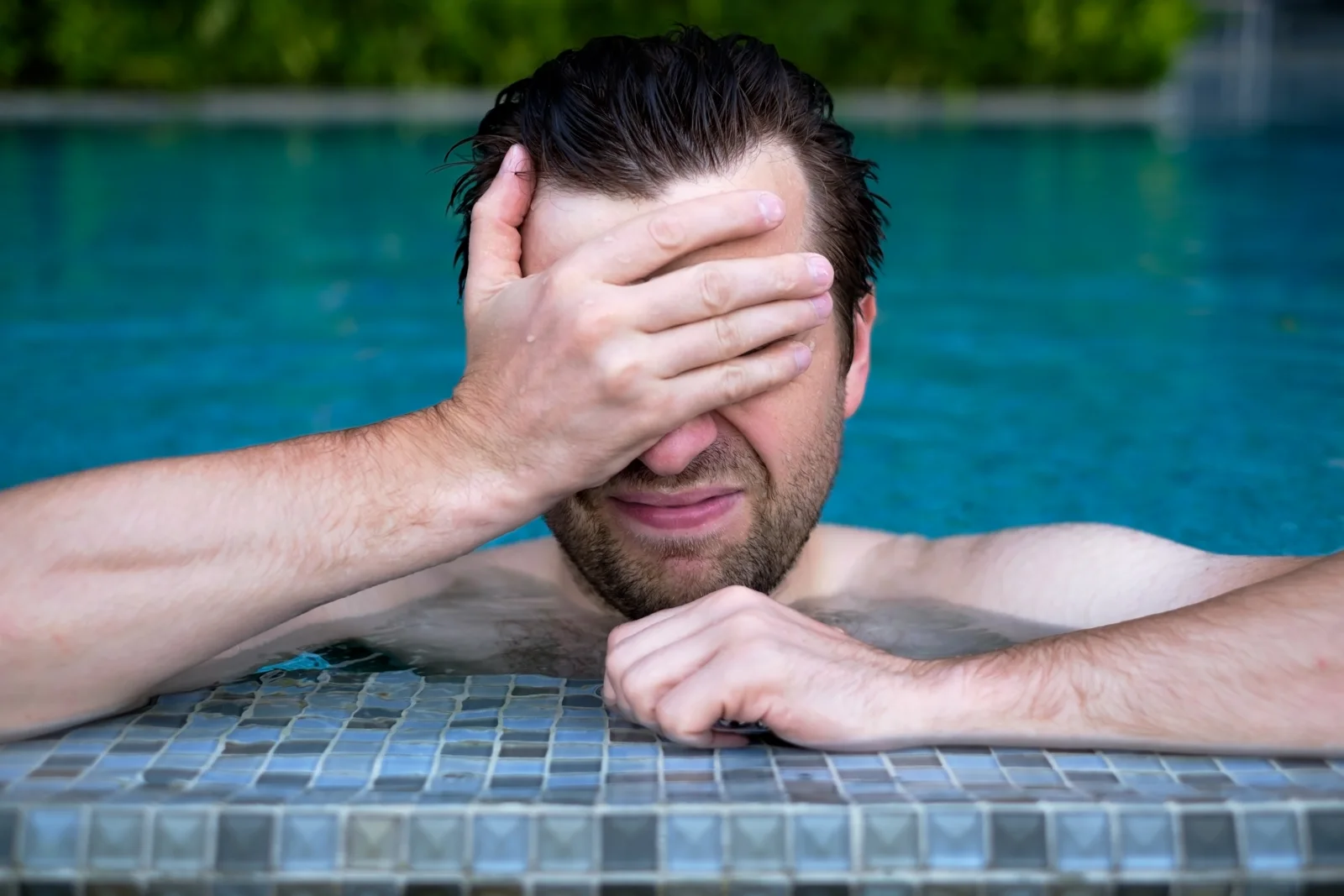 A man in a pool with his hand over his eyes, frustrated
