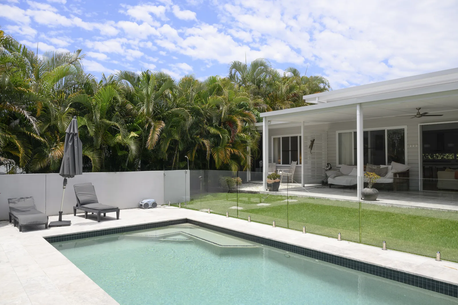 A sunny backyard pool behind a glass fence