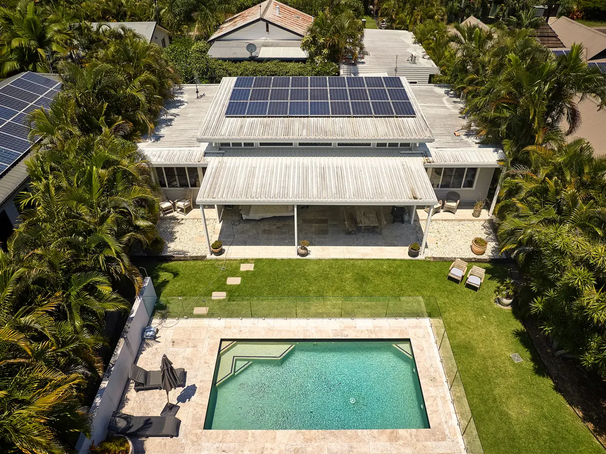 Aerial view of a house with rooftop solar panels and a fenced backyard pool