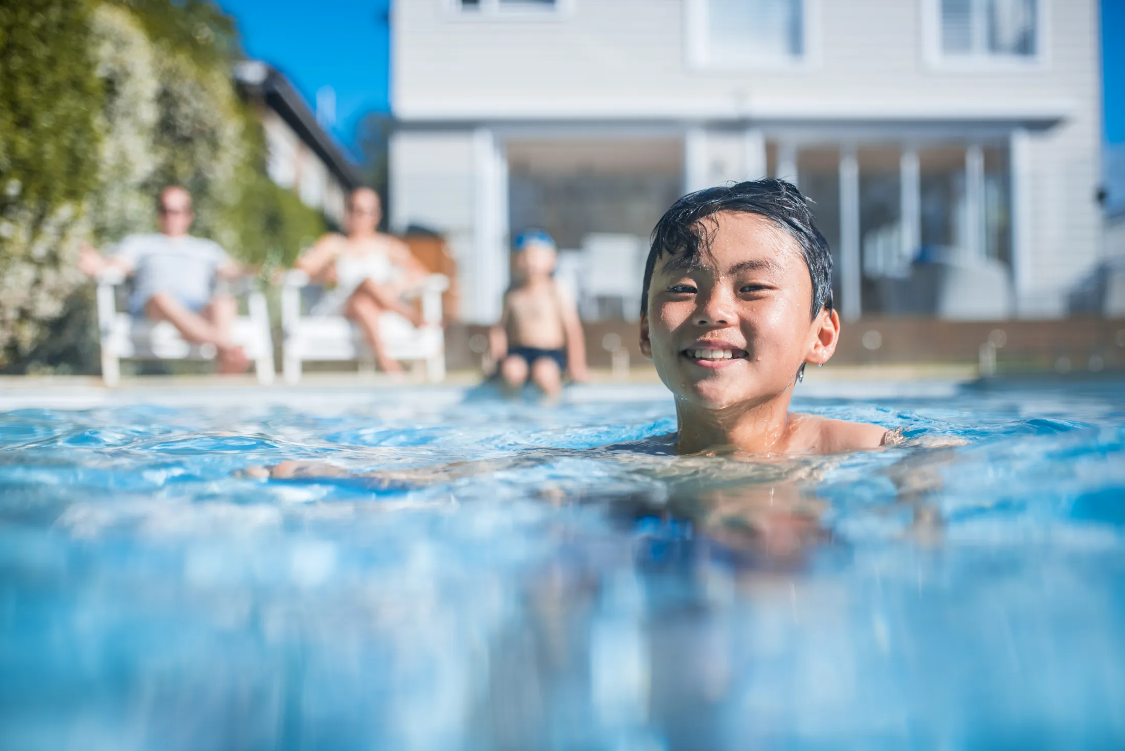 A child swimming in a backyard pool while family relax behind